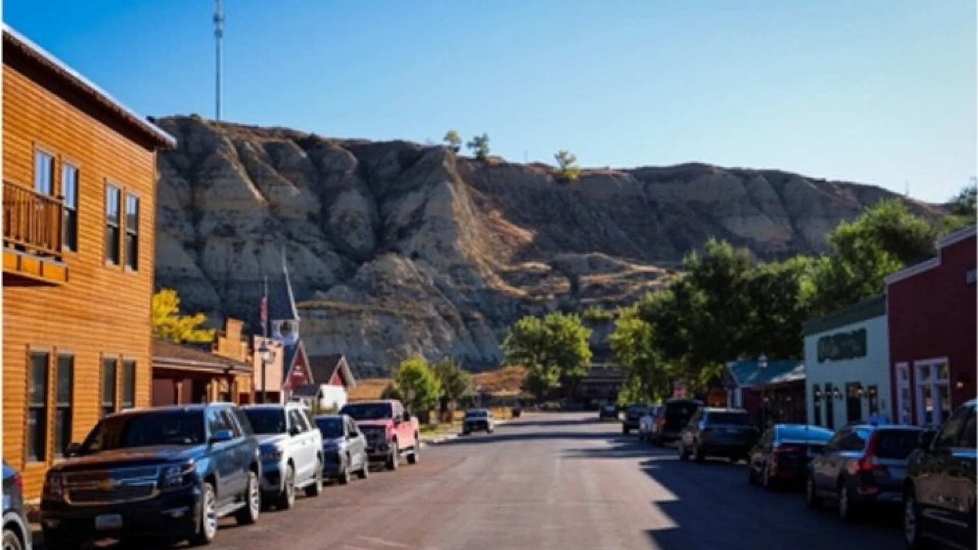 Cars parked along the main street of downtown Medora, North Dakota, with striped badlands bluffs rising behind the storefronts