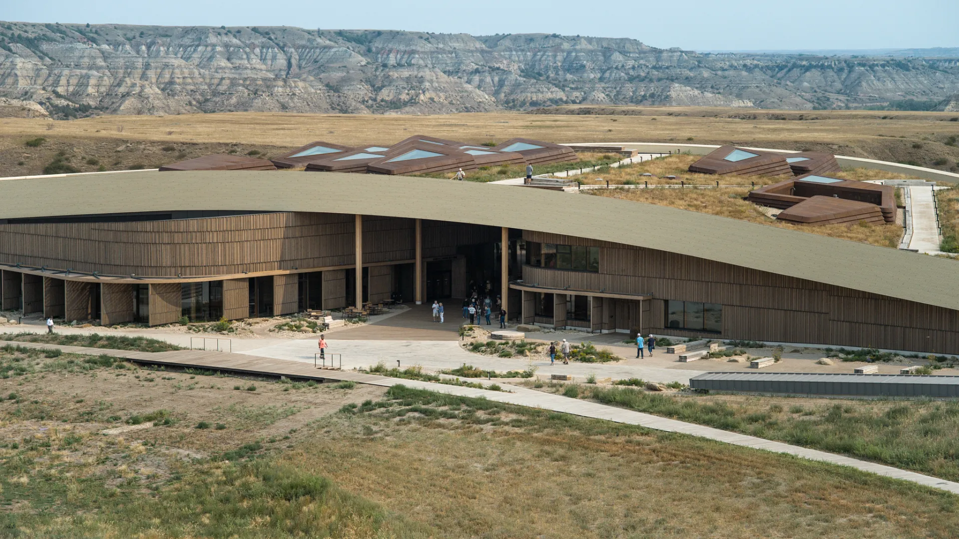 The Theodore Roosevelt Presidential Library, a long curved building with a green roof, set into the grassland with the Badlands buttes behind.