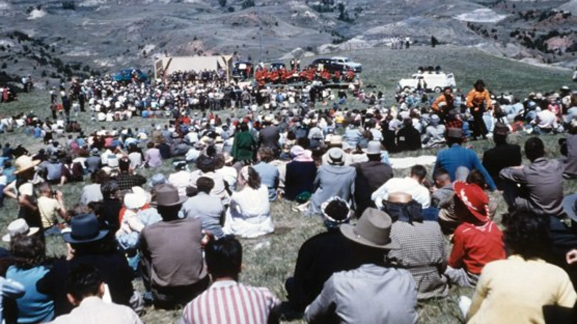 A large crowd seated on a Badlands hillside facing a speakers’ stand.