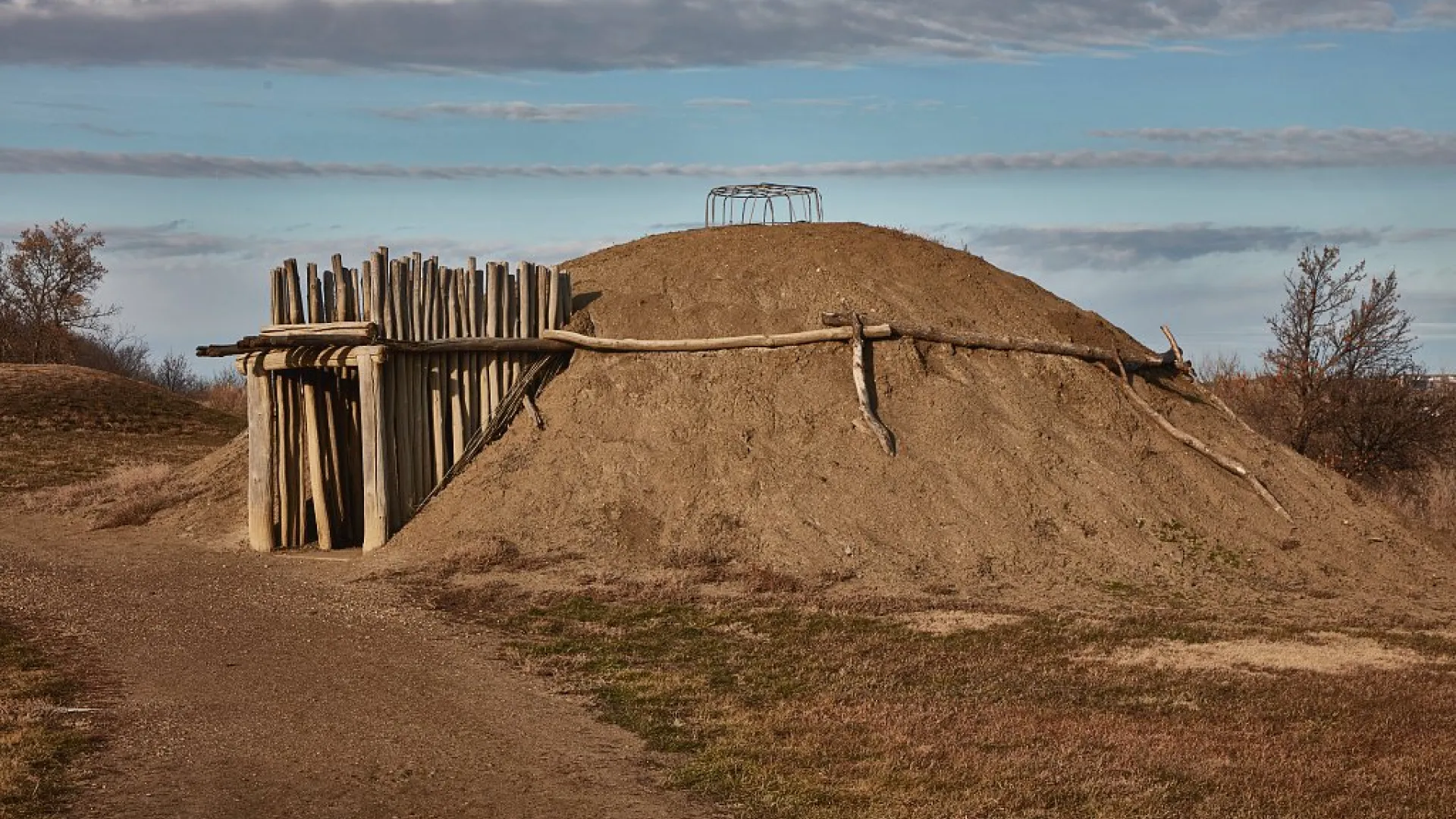 A reconstructed earth-covered lodge with a timber entry passage on a grassy slope.