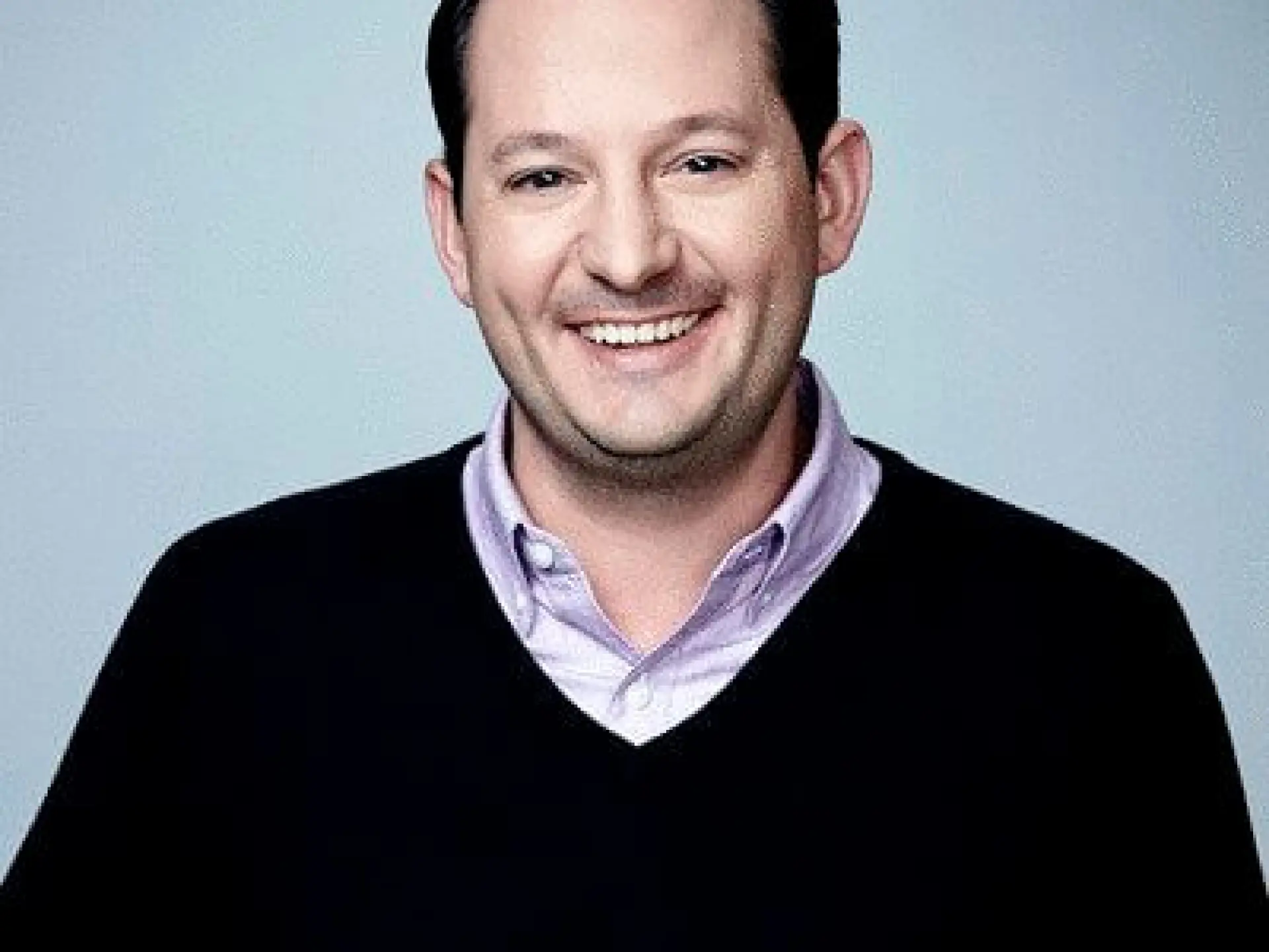Smiling man in a black sweater against a gray background.