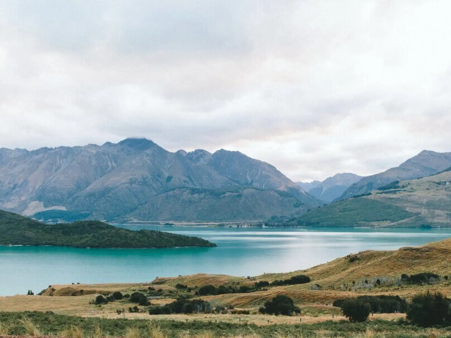 Lake with mountains and grassy hills under a cloudy sky.