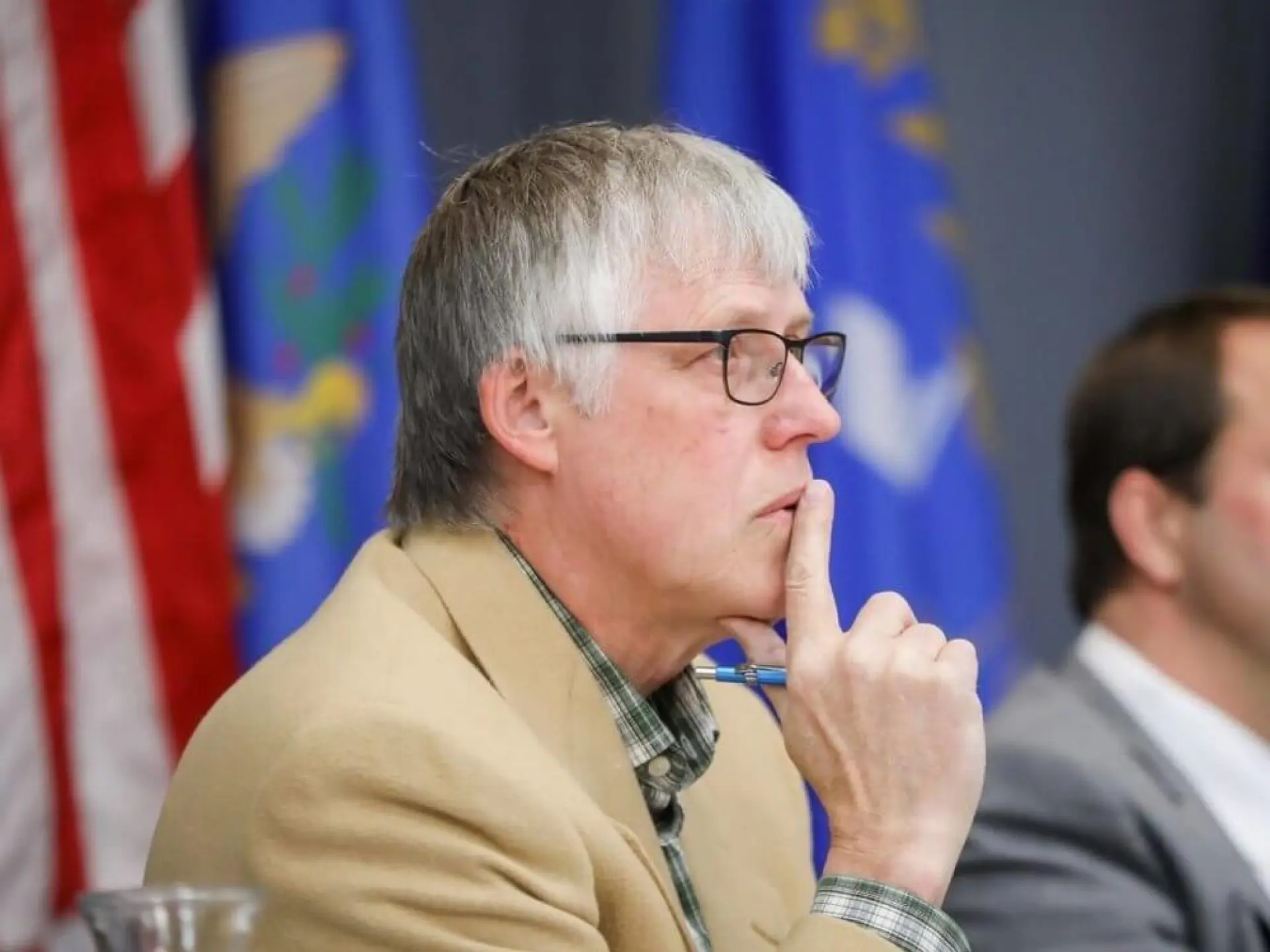 Man in focus, seated, thinking, with flags in the background.