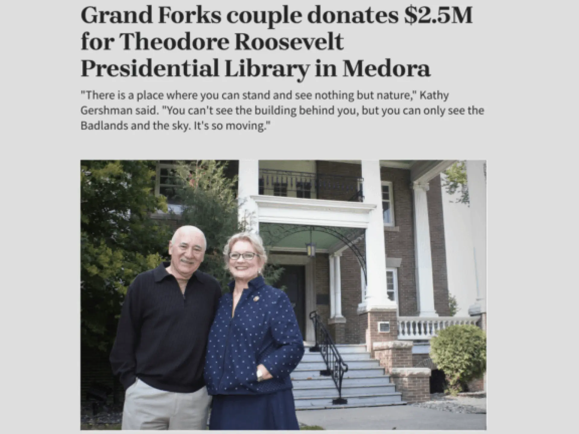 Older couple smiling in front of a large building entrance.