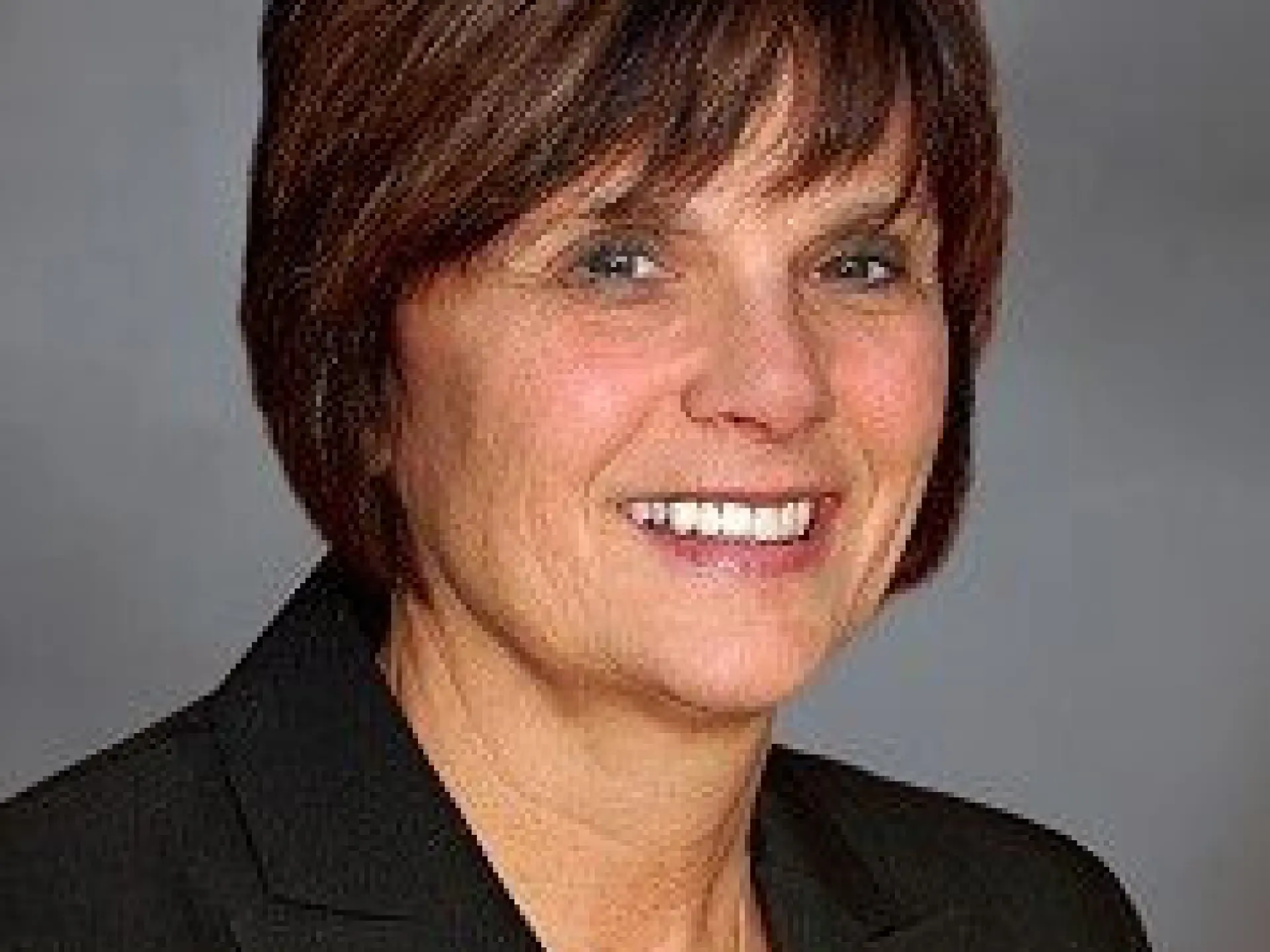 Smiling woman in a suit with short brown hair, gray background.
