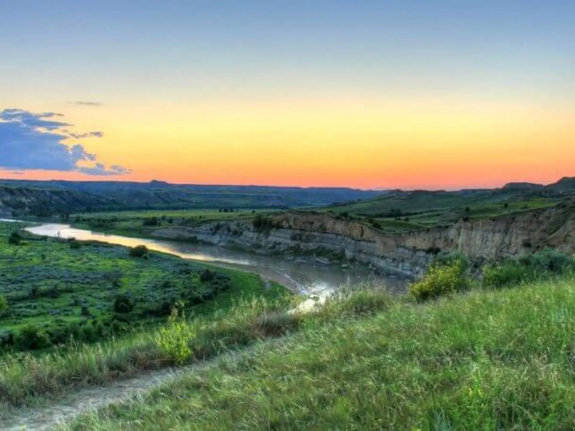 Sunset over a river winding through lush green hills.