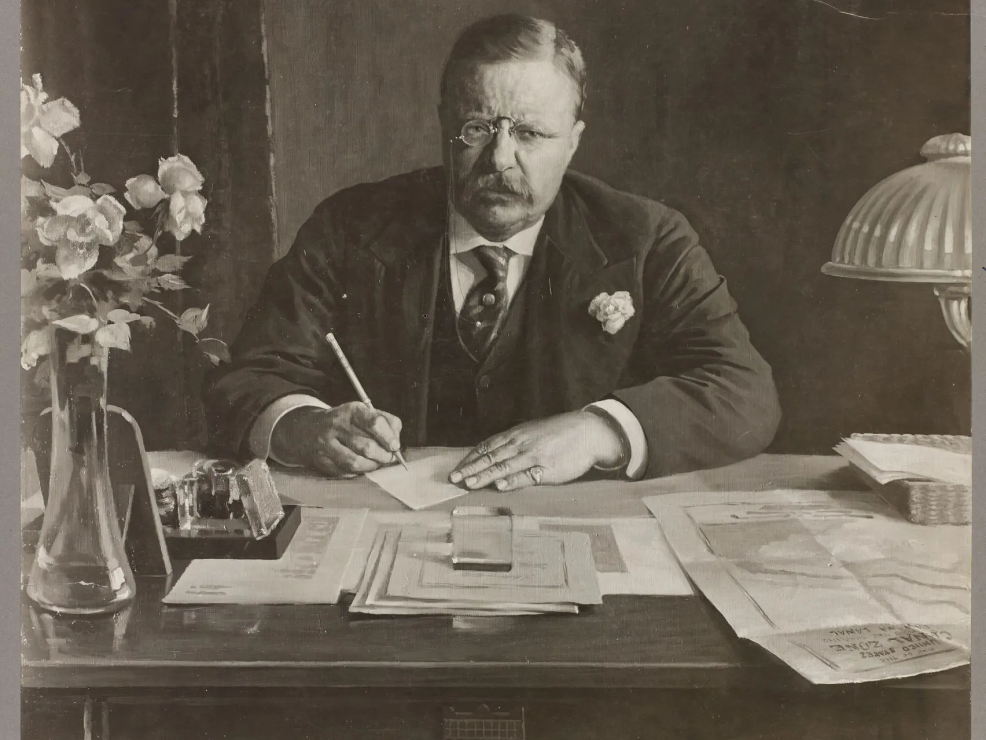 President Theodore Roosevelt seated at his desk writing, in a formal studio portrait