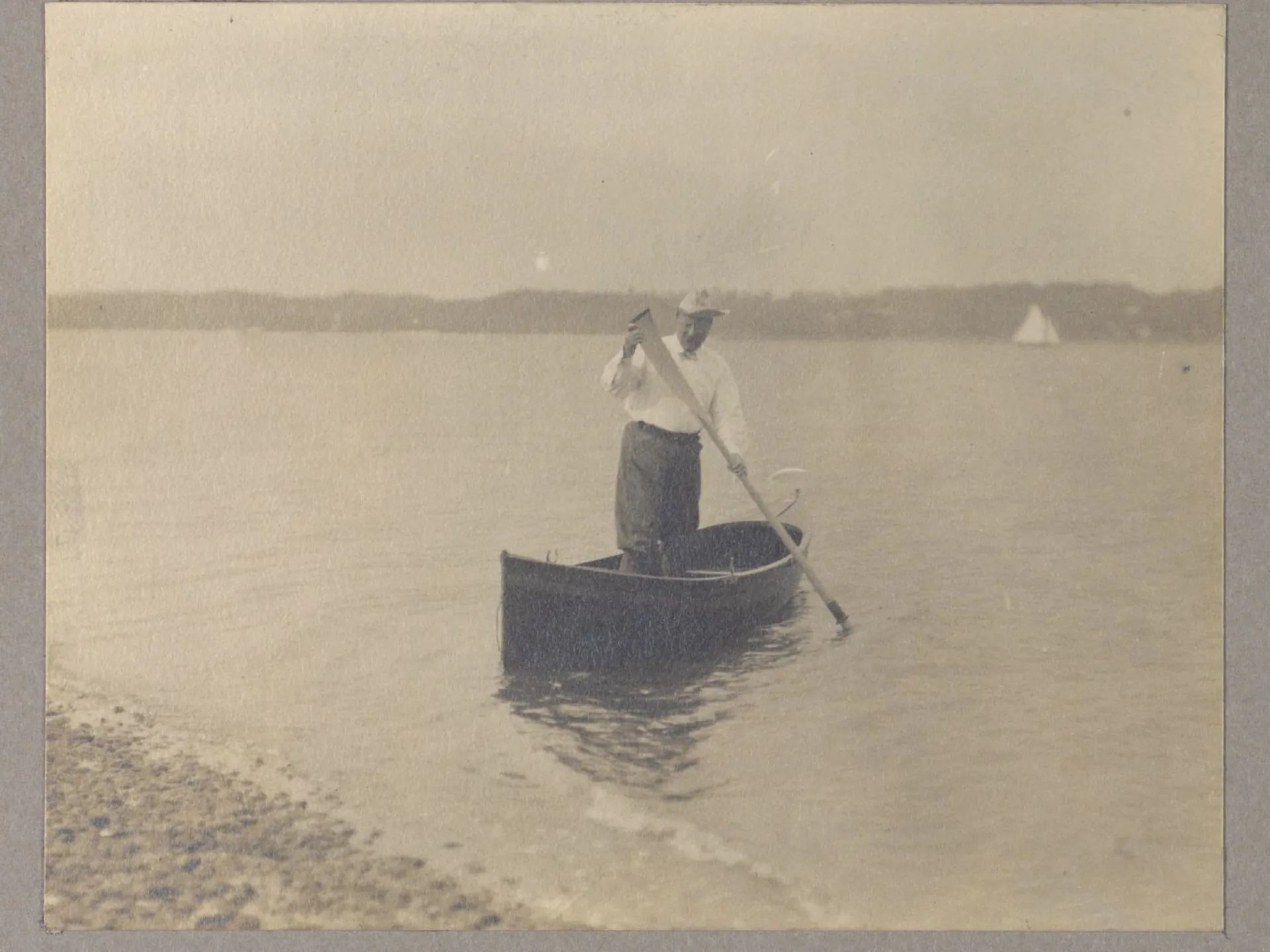 Theodore Roosevelt standing in a canoe and paddling toward shore on open water.