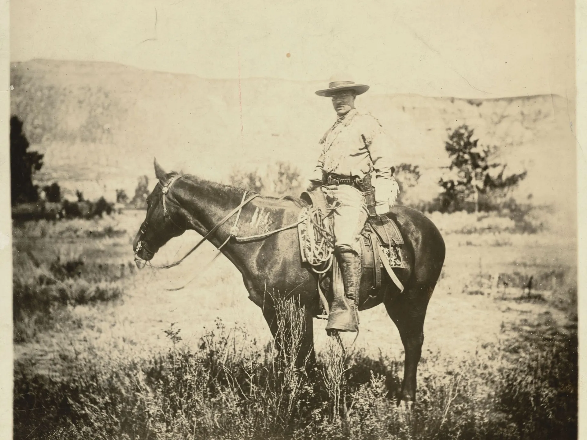 Theodore Roosevelt in ranch clothing mounted on horseback in the Dakota Badlands