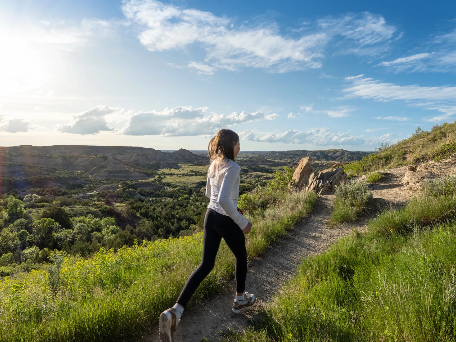 A visitor walking a grassy trail along the rim above the badlands in Theodore Roosevelt National Park
