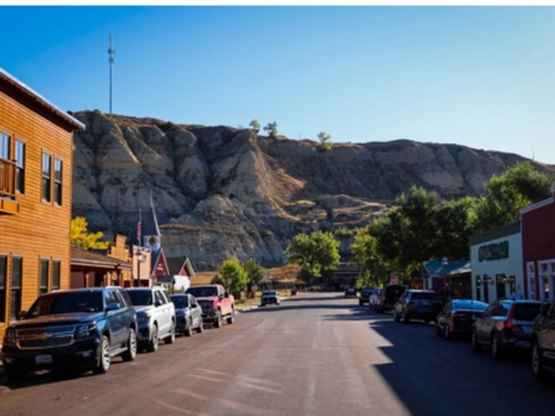 Cars parked along the main street of downtown Medora, North Dakota, with striped badlands bluffs rising behind the storefronts
