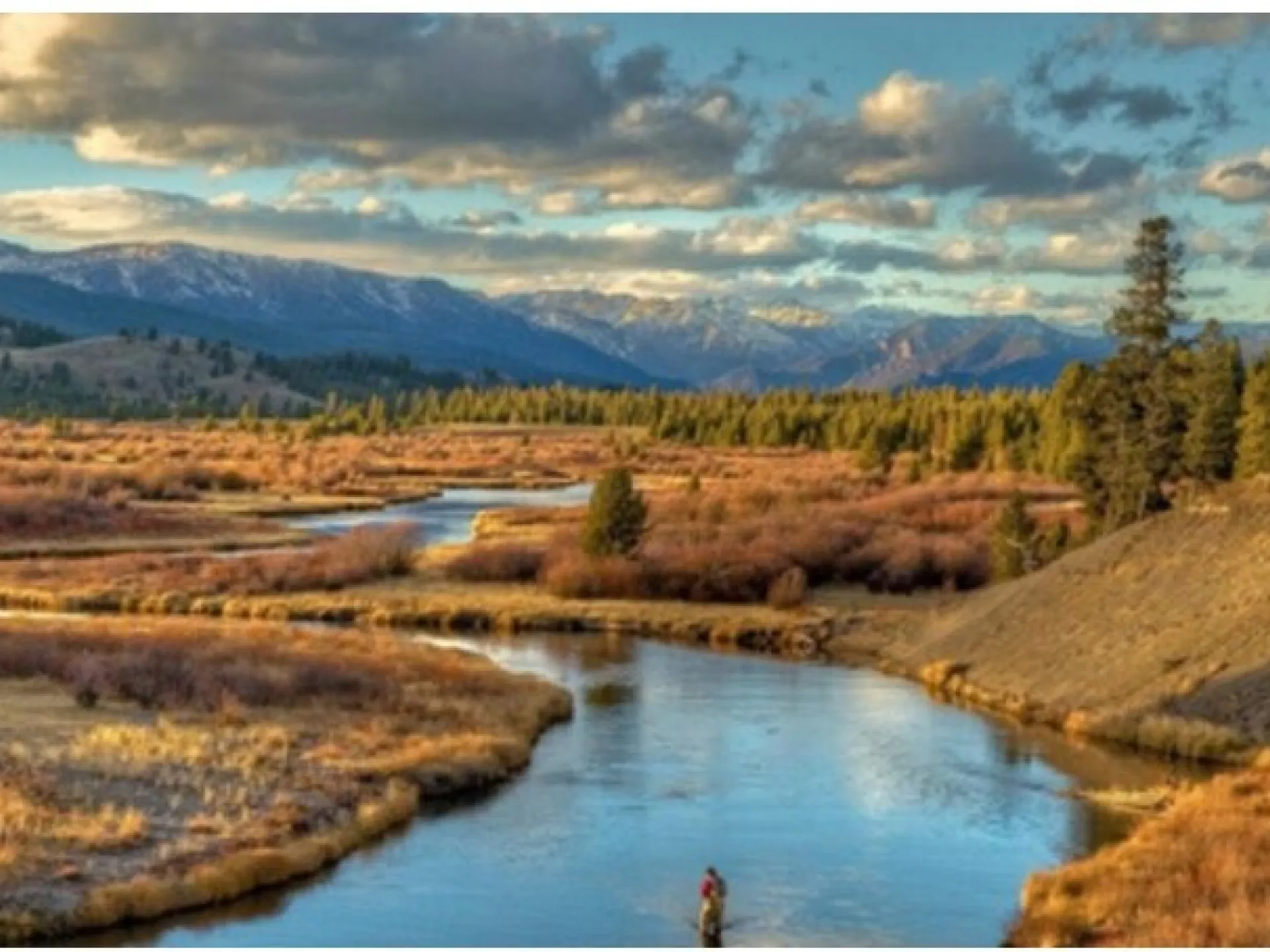The Yellowstone River winding through open valley below snow-capped mountains near West Yellowstone, Montana