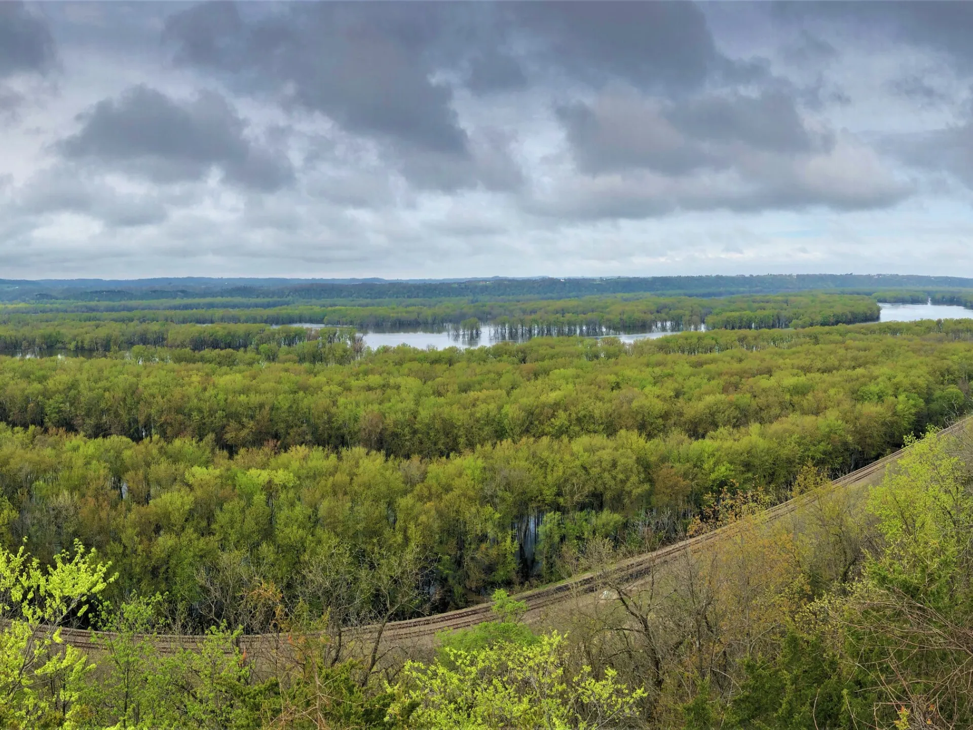 View from a bluff over the wooded floodplain and open water of the Upper Mississippi River under a cloudy sky