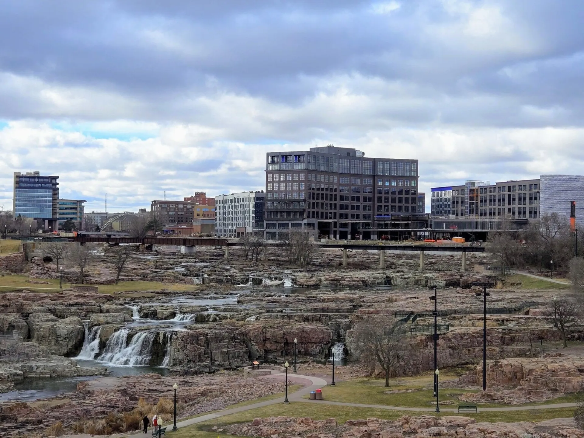 The Big Sioux River dropping over pink quartzite at Falls Park with downtown Sioux Falls behind