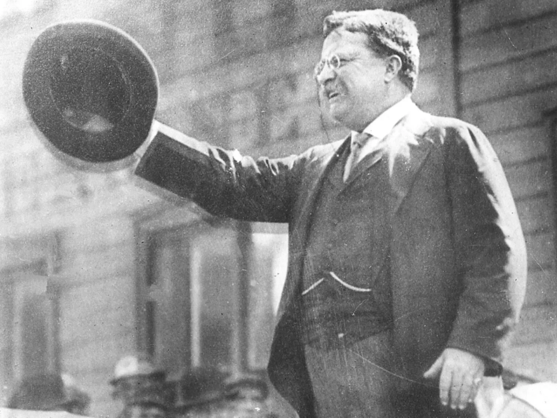 Roosevelt waving his hat to a crowd from an open car
