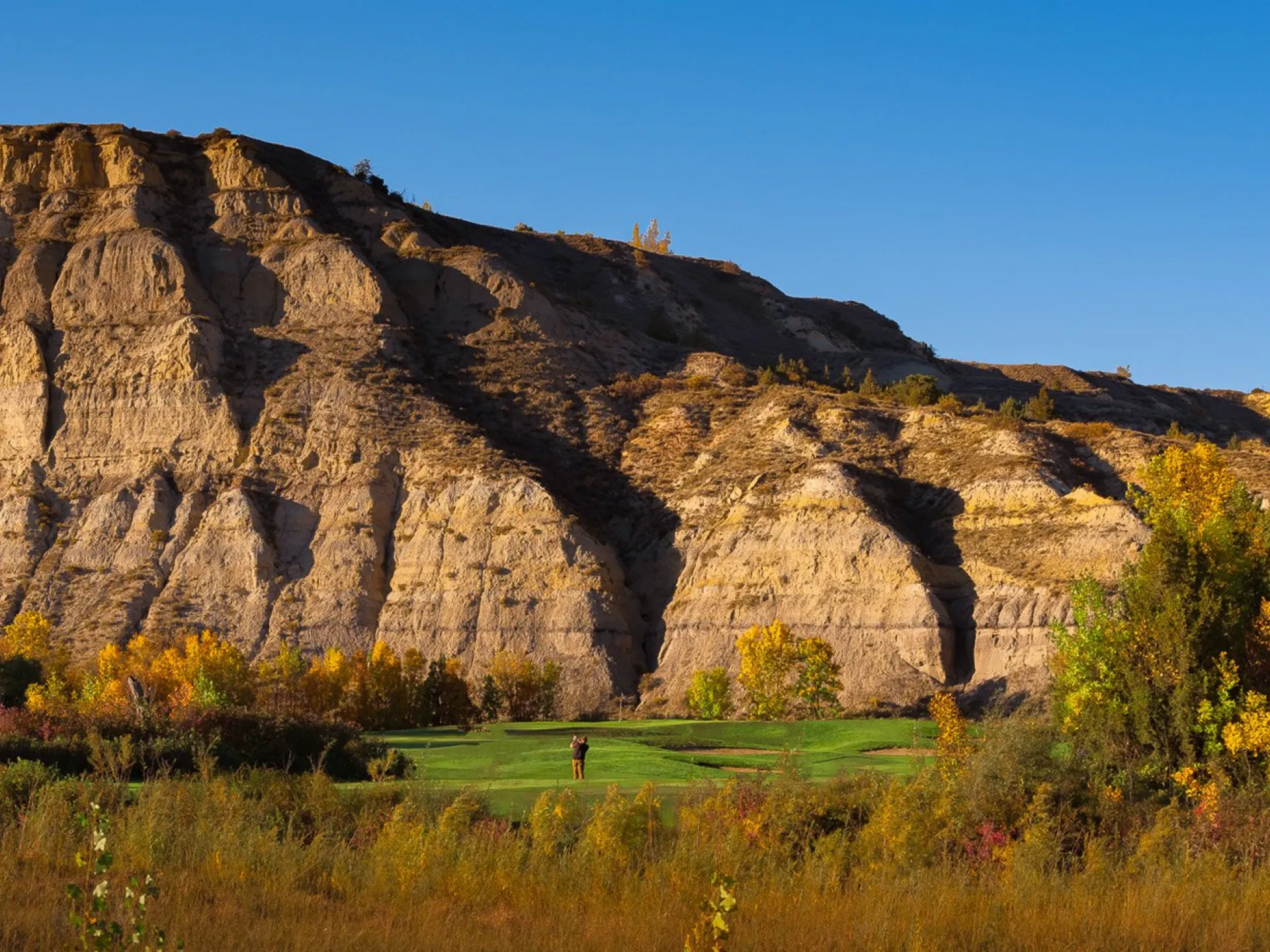 Butte rising above a green at Bully Pulpit Golf Course in fall color