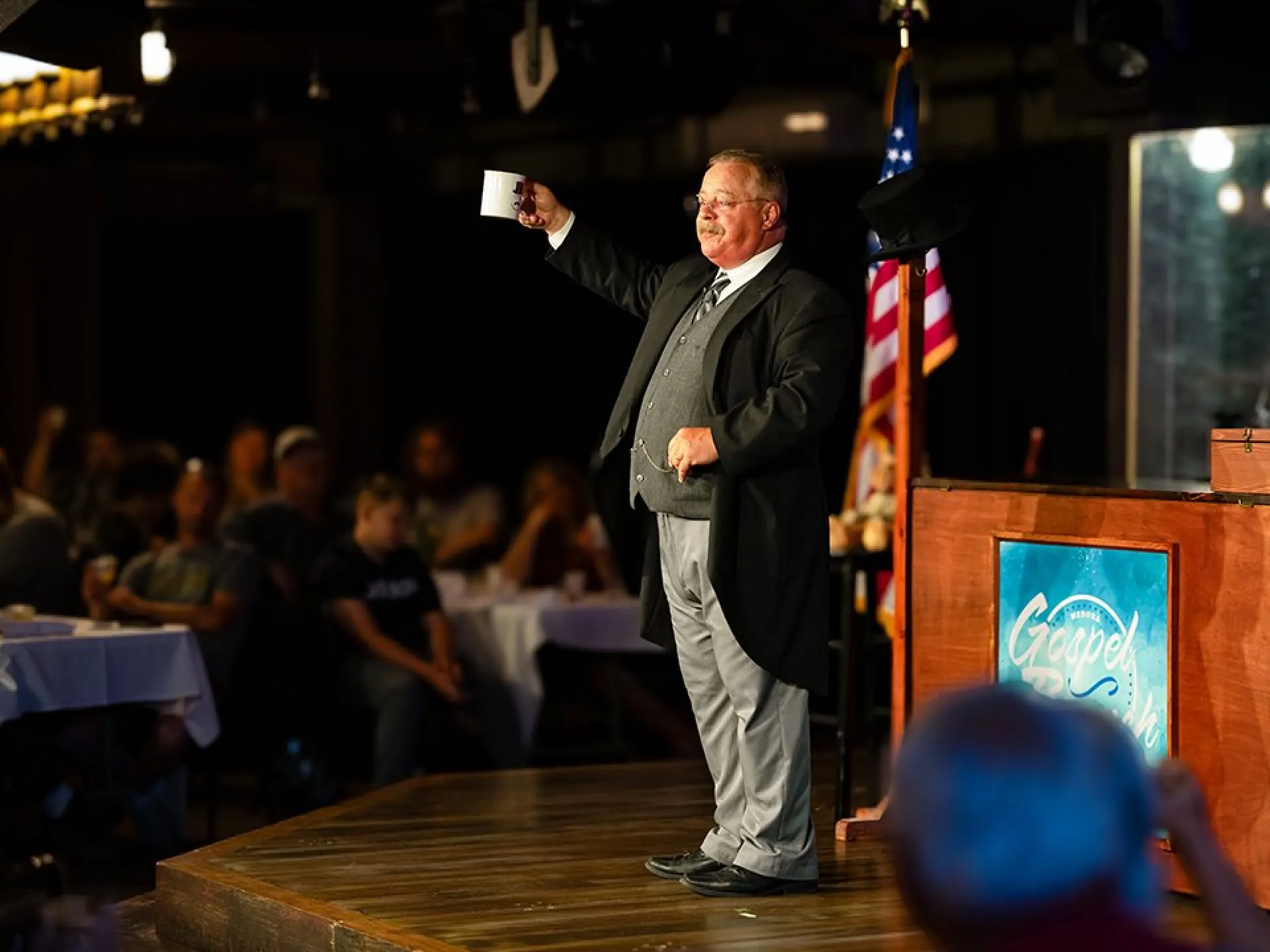 Theodore Roosevelt portrayer raising a mug on stage