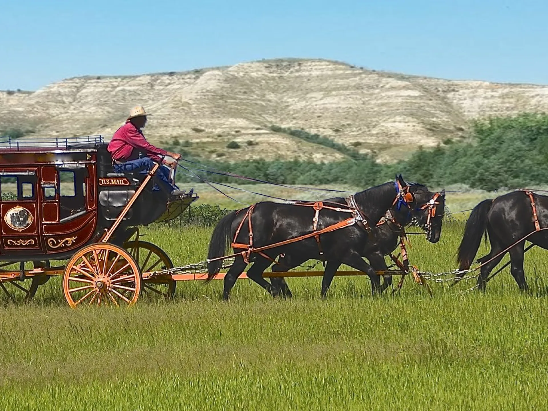 Red stagecoach and four-horse team crossing Badlands grassland