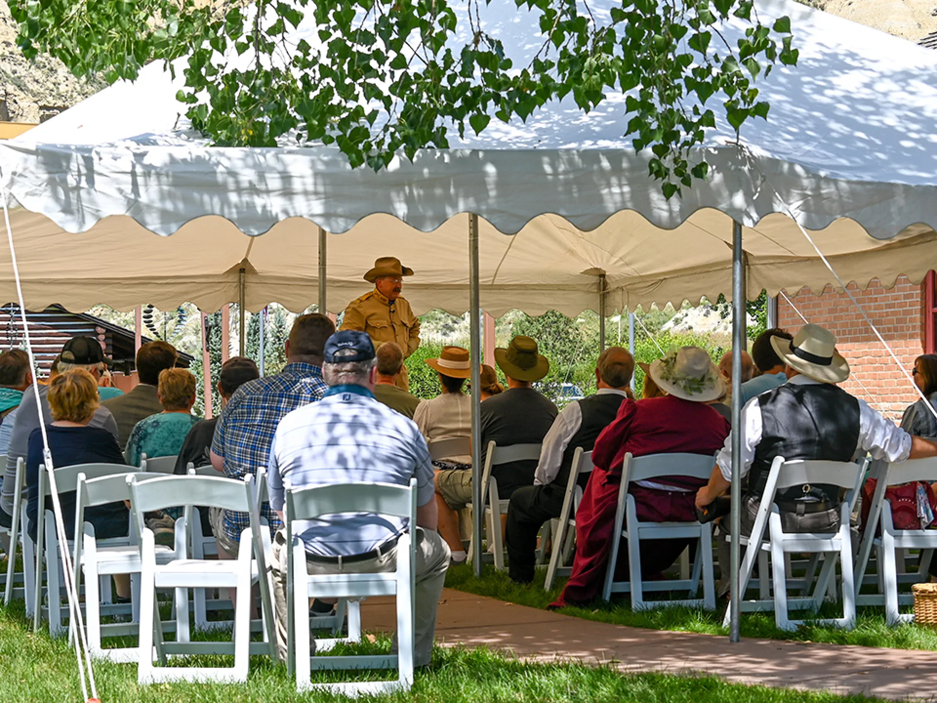 An audience under a white tent listens to a Roosevelt interpreter in a campaign hat
