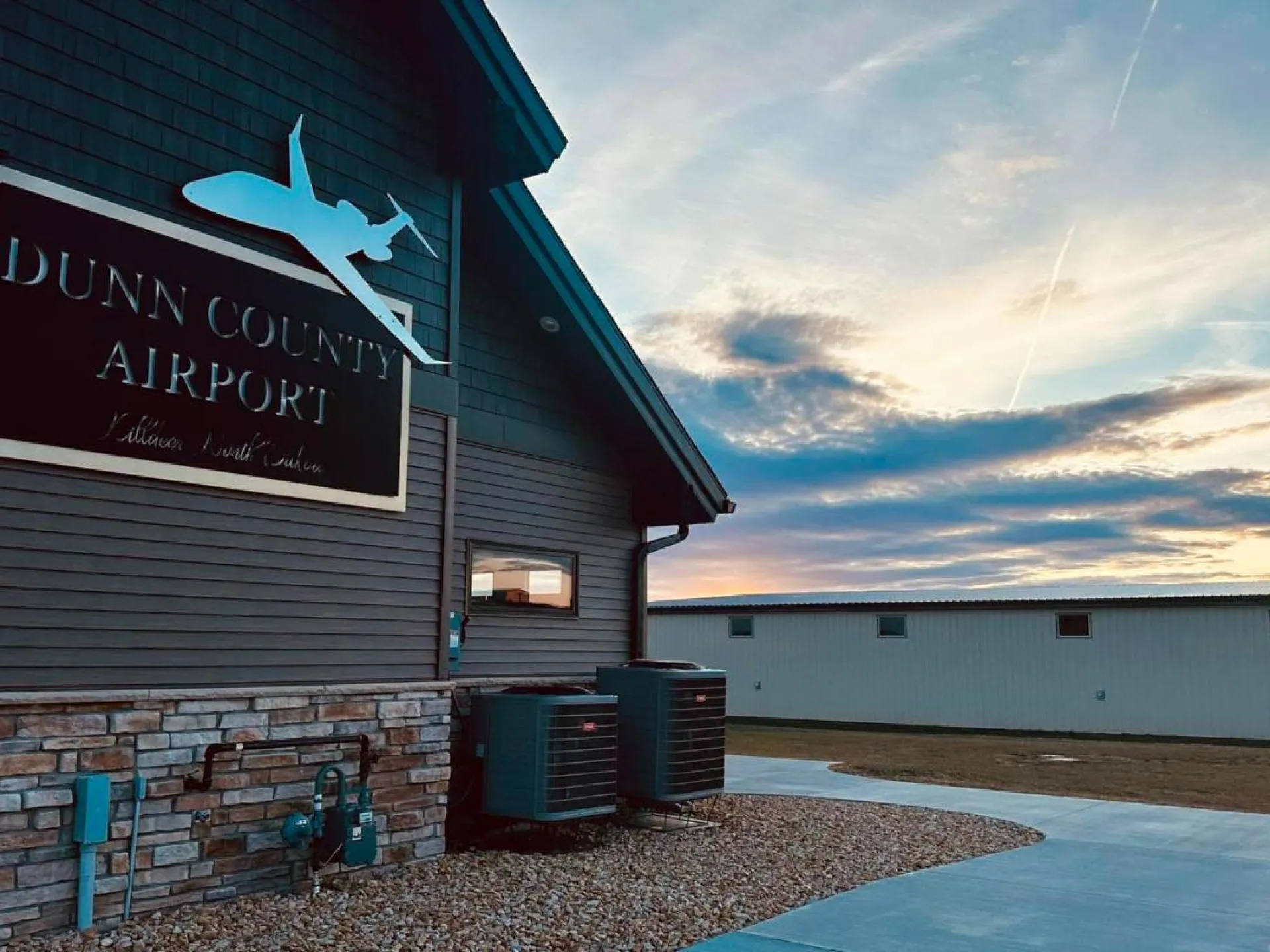 The Dunn County Airport terminal and pilot lounge near Killdeer at sunset, with a hangar beyond