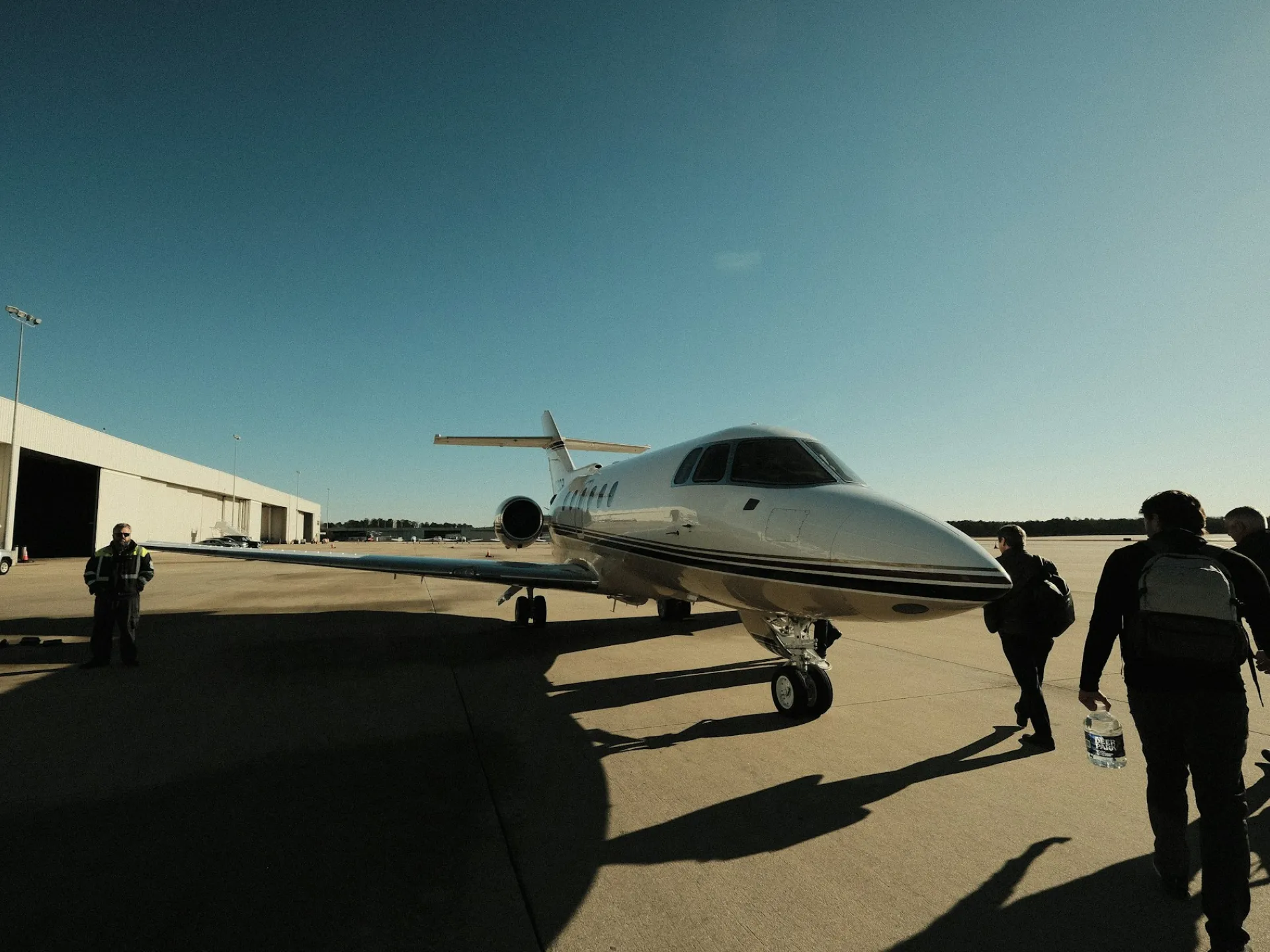 Passengers walk across an airport ramp toward a parked business jet