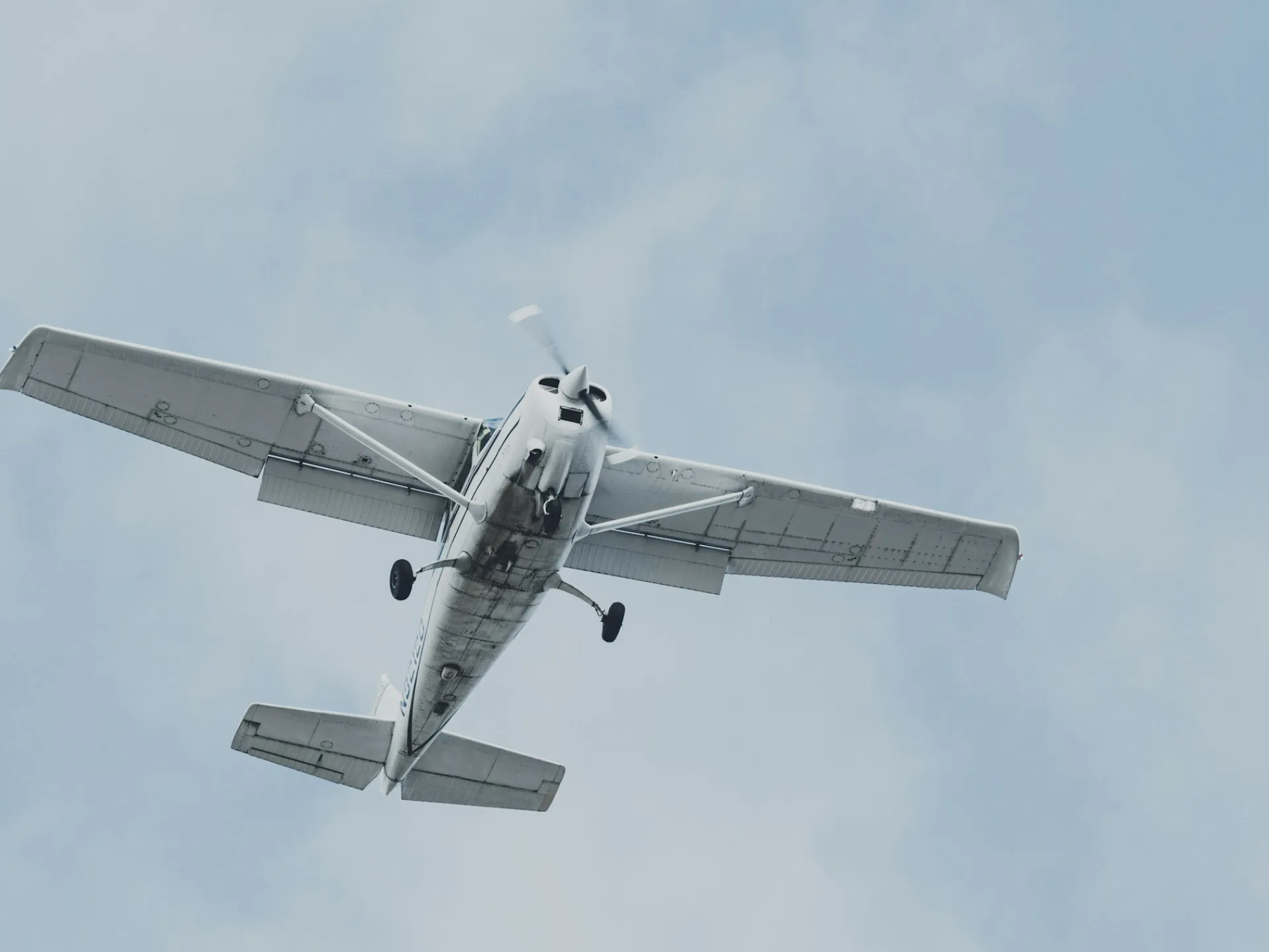 A Cessna 172 seen from below on short final, against a pale sky