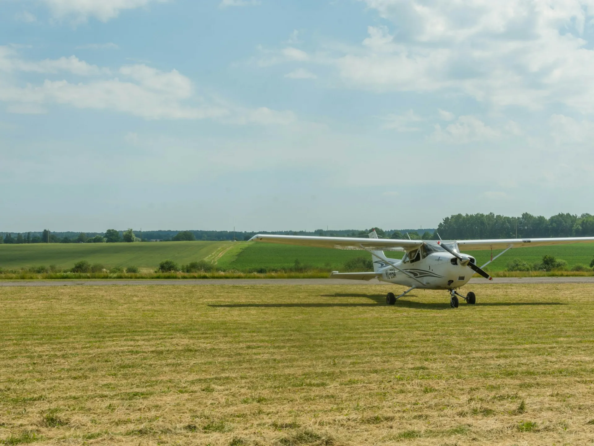A small high-wing plane sits on a grass airstrip under a wide sky