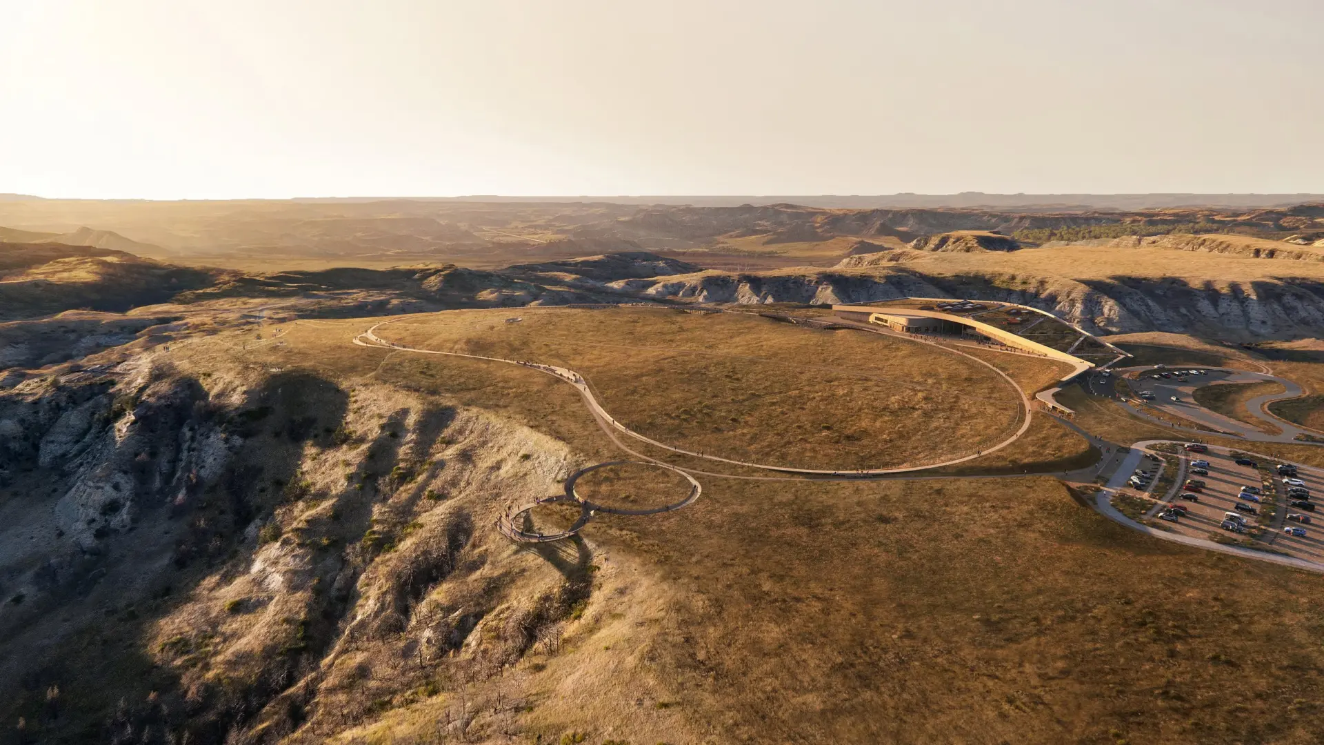 Aerial view of a vast, sunlit landscape with winding dirt paths and hills.