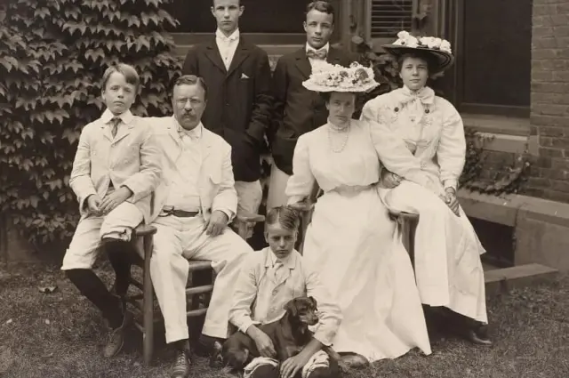 Family photo in garden, early 1900s attire, three seated, four standing, formal expressions.