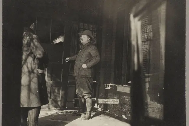 Man in winter attire talking to another outdoors, casting long shadows.