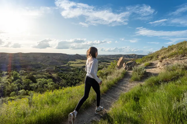 A visitor walking a grassy trail along the rim above the badlands in Theodore Roosevelt National Park