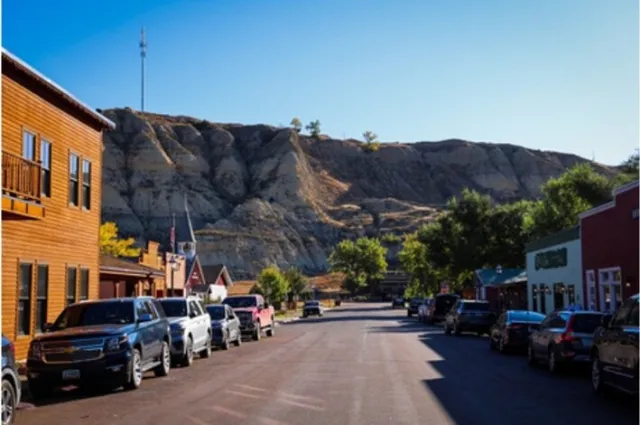 Cars parked along the main street of downtown Medora, North Dakota, with striped badlands bluffs rising behind the storefronts