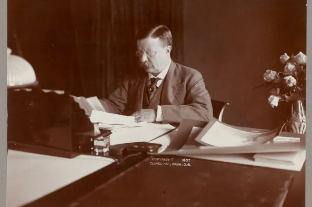 President Theodore Roosevelt seated at his desk reviewing papers