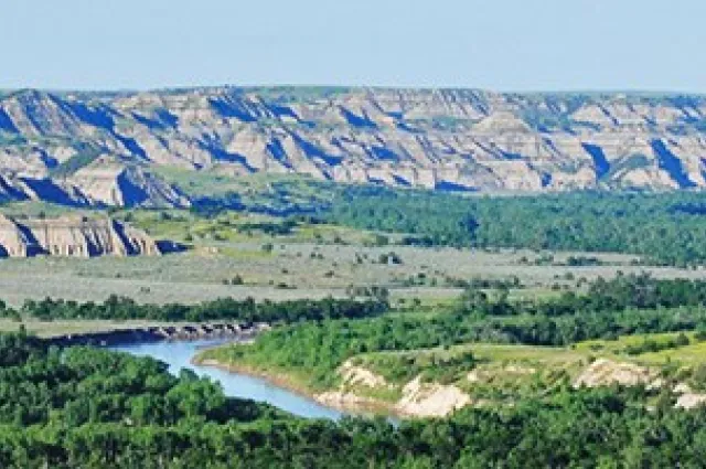 Tan and grey striped buttes rise above a green river valley in the North Unit of Theodore Roosevelt National Park