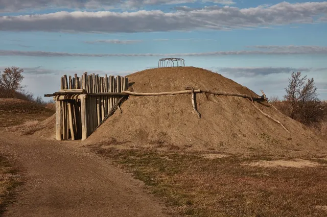 A reconstructed earth-covered lodge with a timber entry passage on a grassy slope.