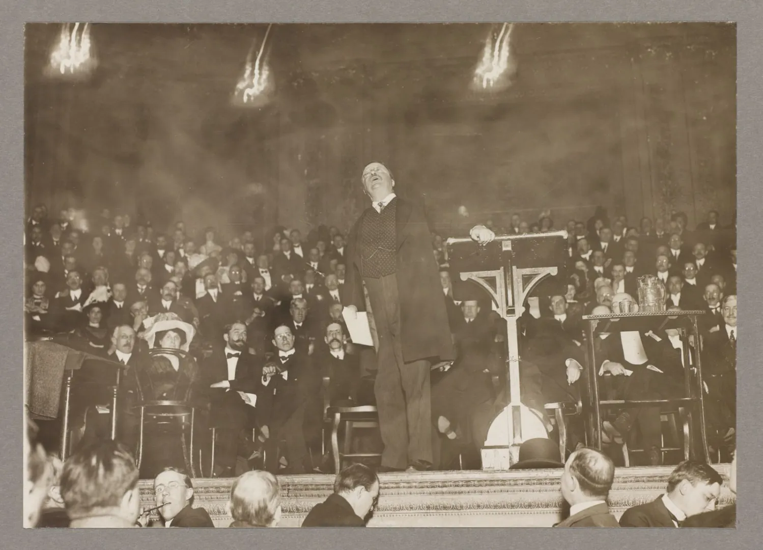 Theodore Roosevelt speaking from a platform to a densely packed convention hall in 1912