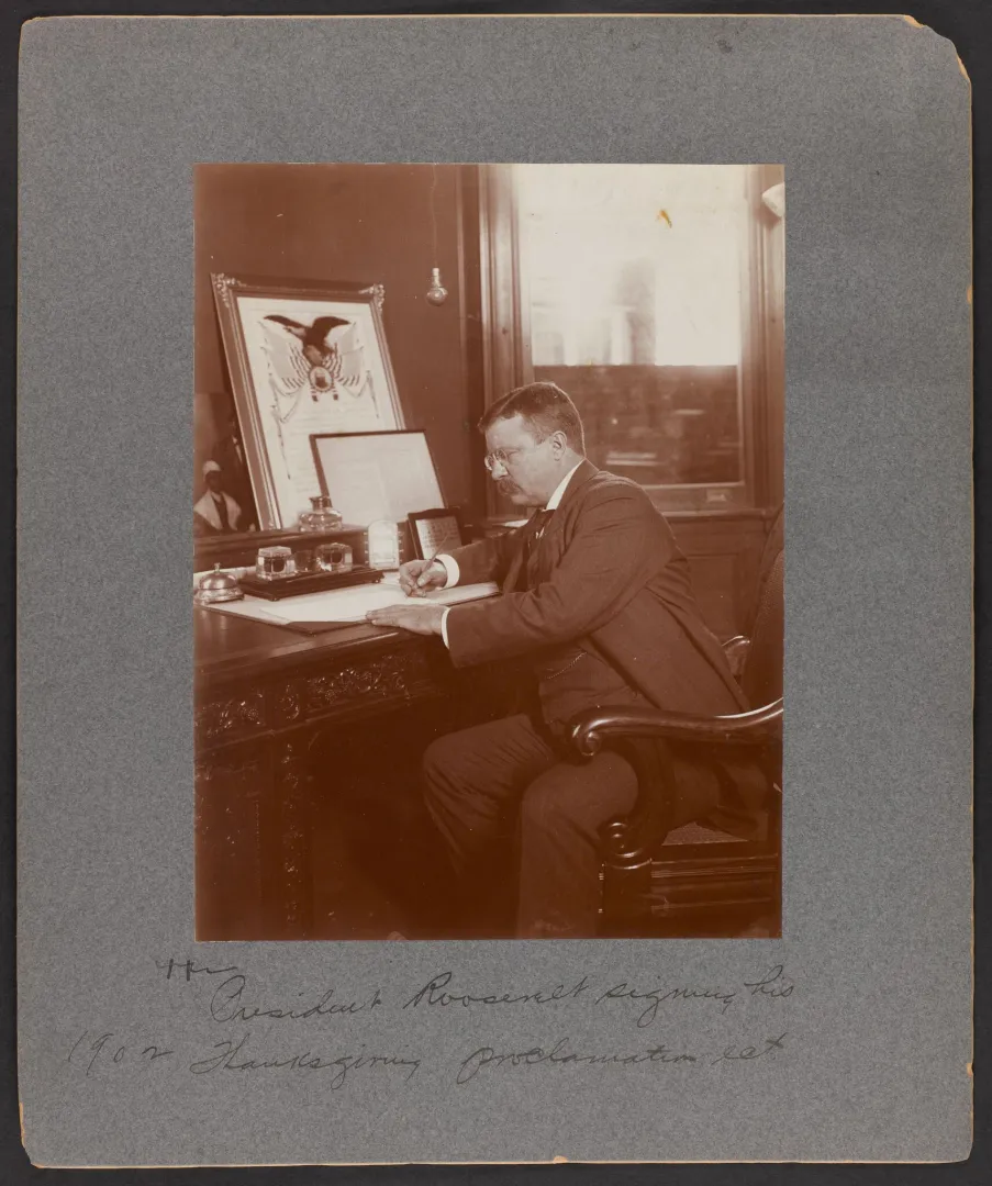 President Theodore Roosevelt seated at a desk signing a document in 1902