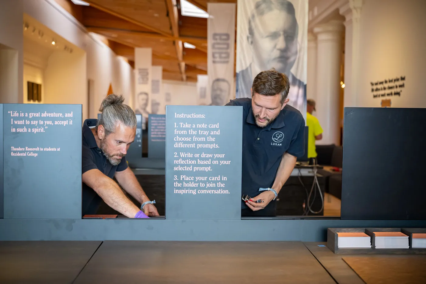 Visitors engage with an interactive exhibit beneath a large portrait of Theodore Roosevelt