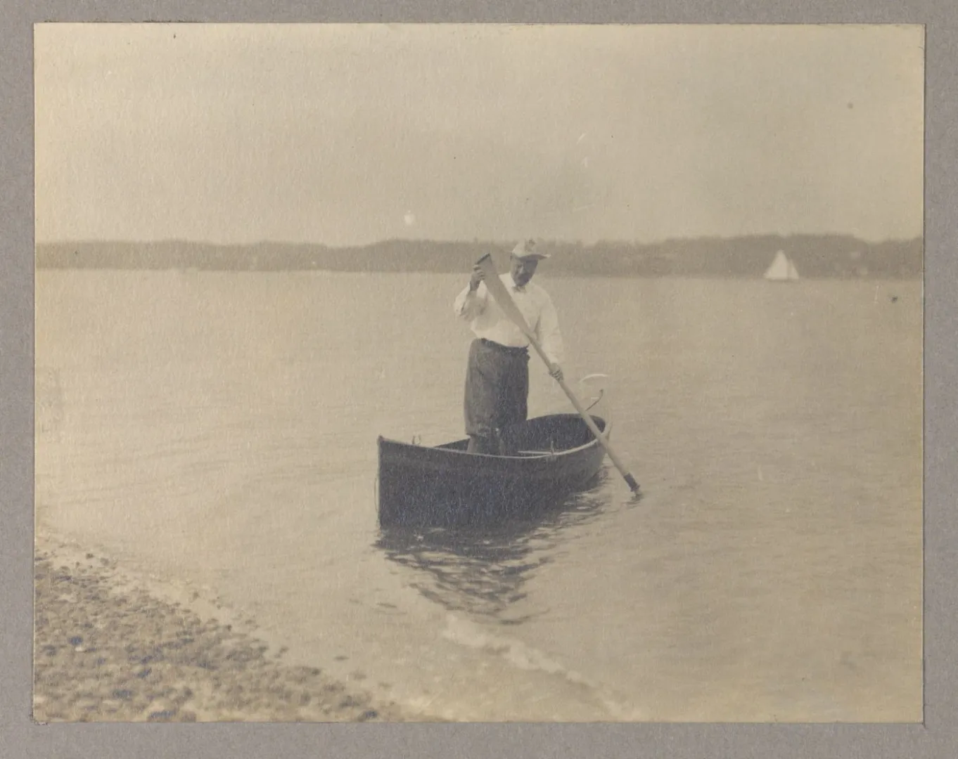 Theodore Roosevelt standing in a canoe and paddling toward shore on open water.
