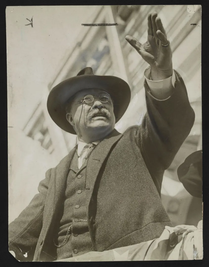 Theodore Roosevelt in a hat with his hand raised, speaking passionately to a crowd at Hackensack, New Jersey, in 1912
