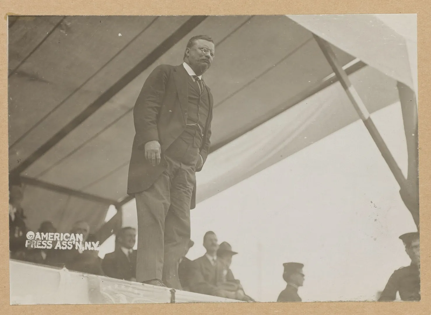 Theodore Roosevelt standing on a platform speaking, with a seated audience behind him