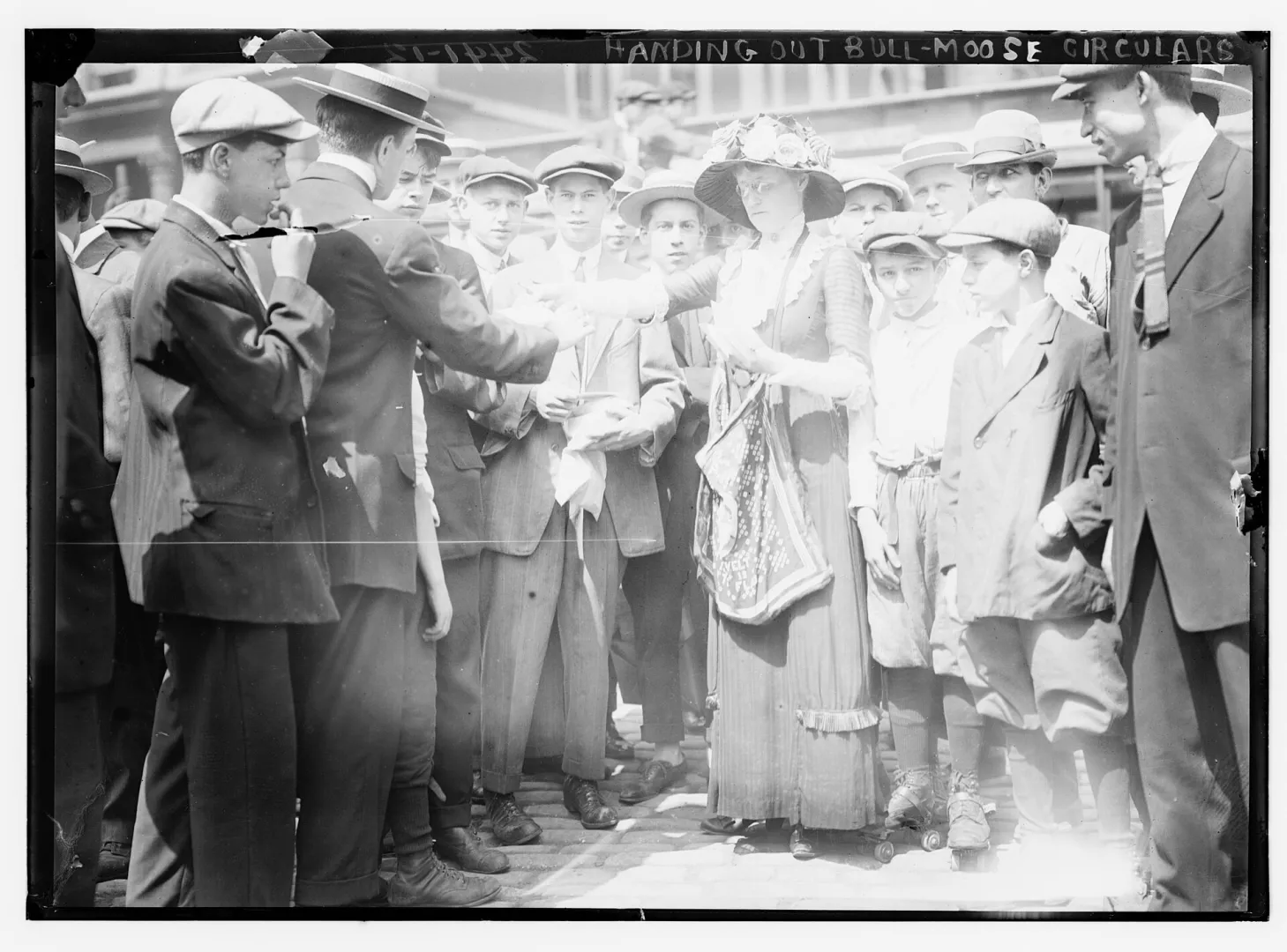 A crowd on a city street gathered as Bull Moose campaign circulars are handed out in 1912