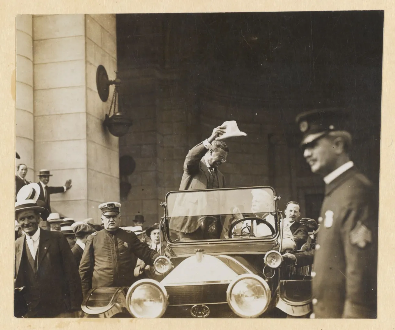President Theodore Roosevelt standing in an open automobile amid a crowd