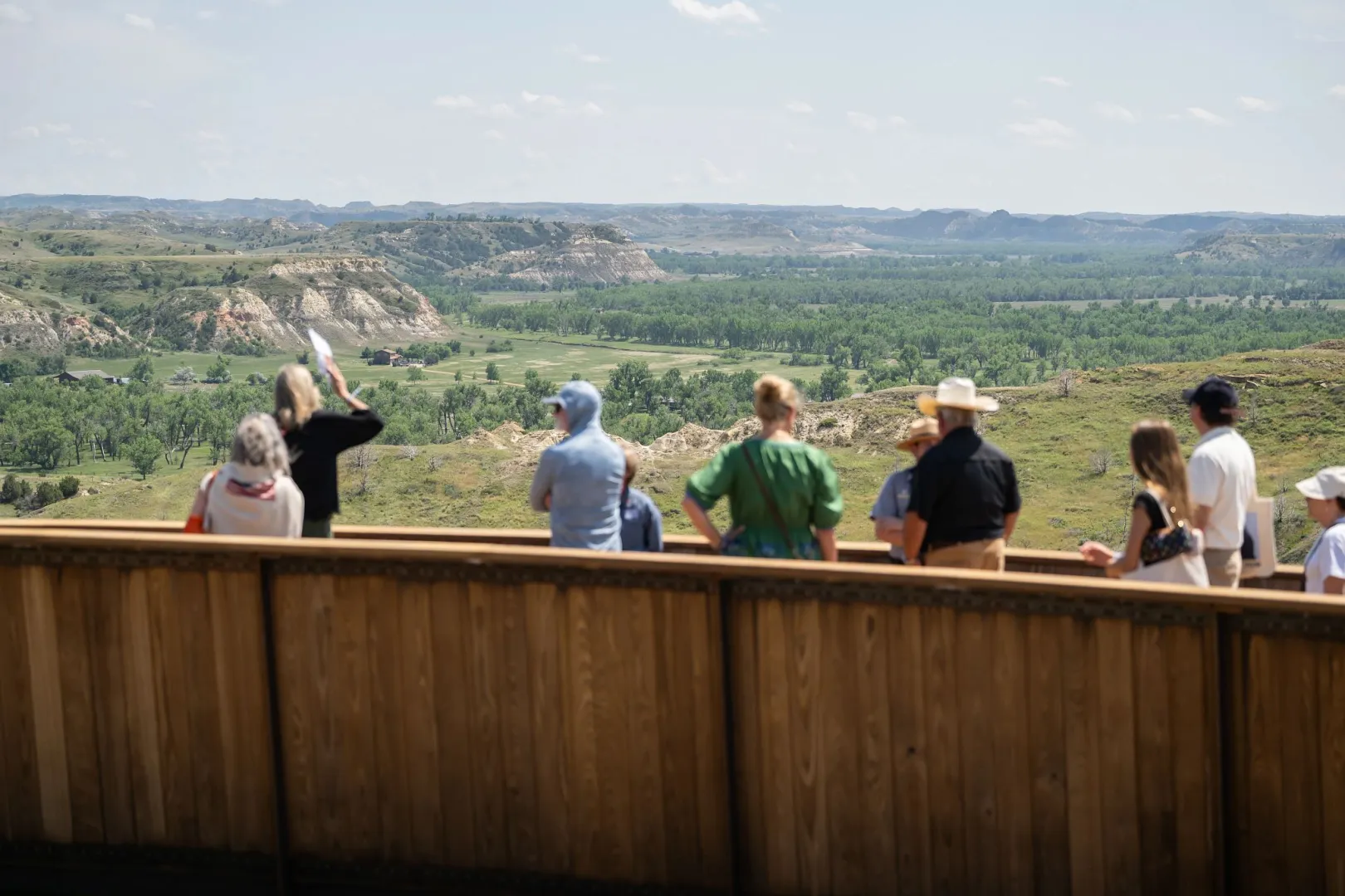 Visitors at a railing overlook taking in a broad badlands vista