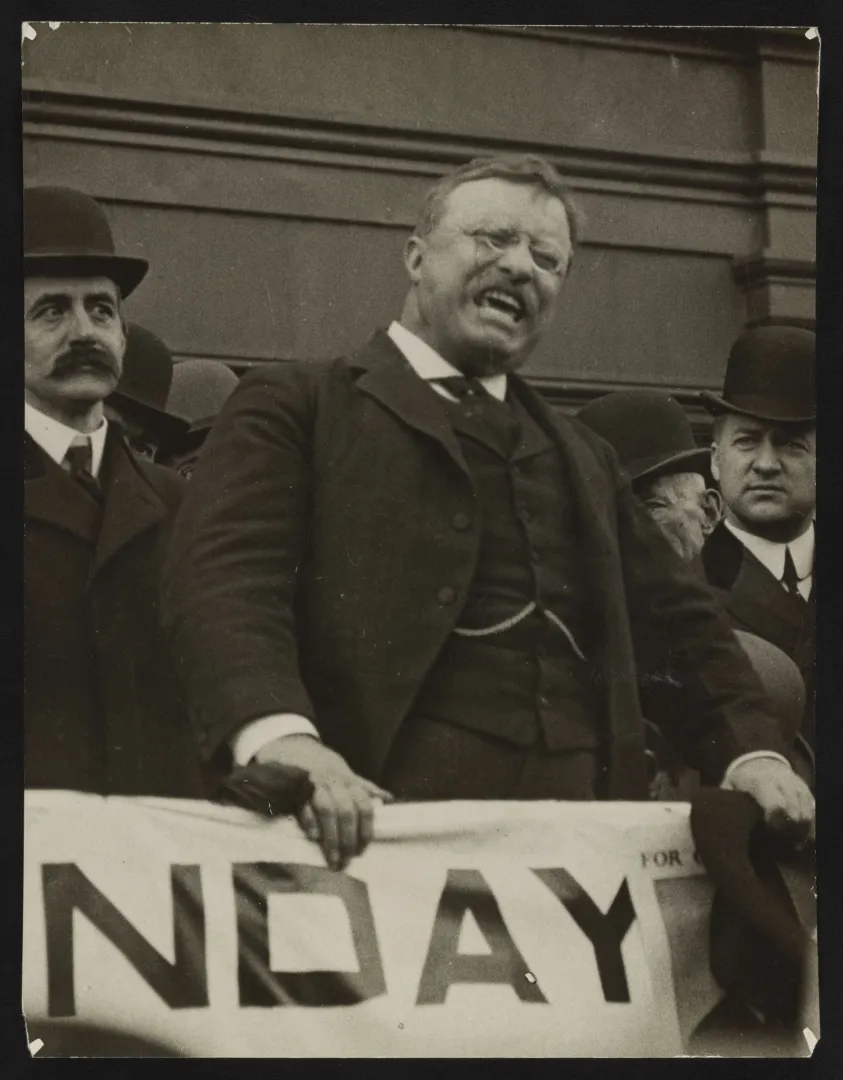 Theodore Roosevelt leaning forward and speaking intensely from a platform