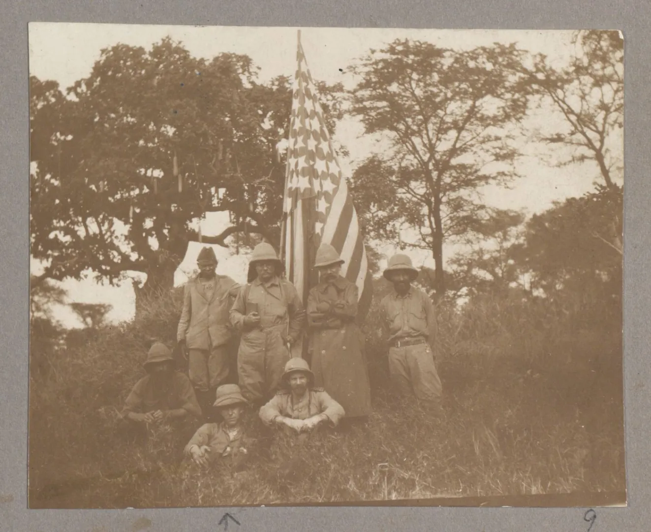 Theodore Roosevelt with members of his safari party gathered beside an American flag in Africa.