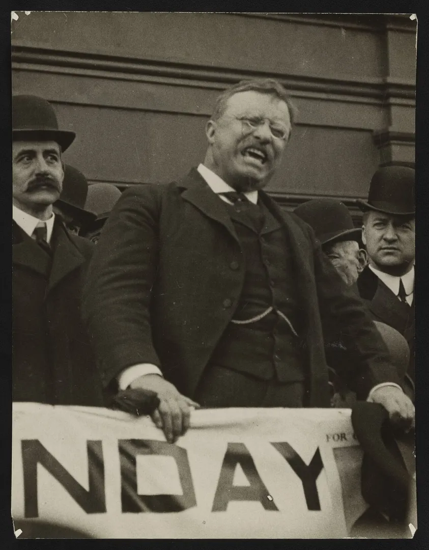 Theodore Roosevelt gesturing emphatically while delivering a speech from a platform