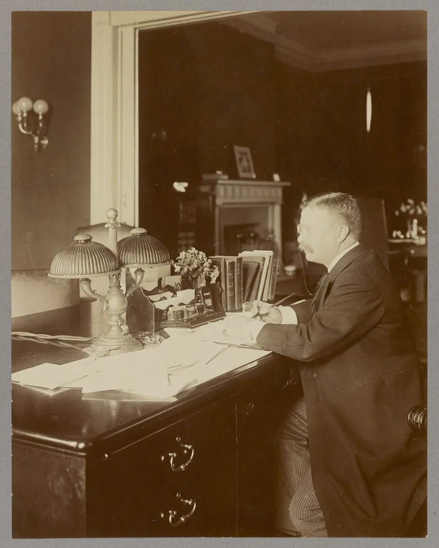 Theodore Roosevelt seated writing at his desk