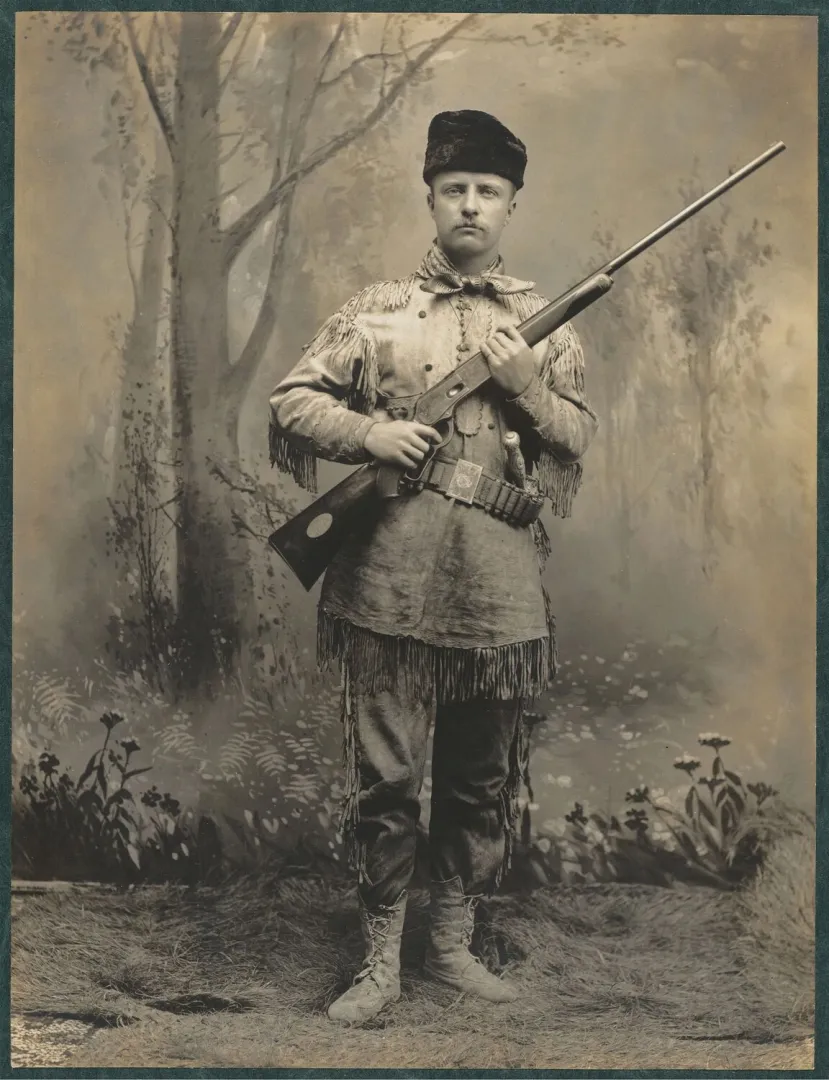 Theodore Roosevelt standing in a buckskin hunting suit holding a rifle