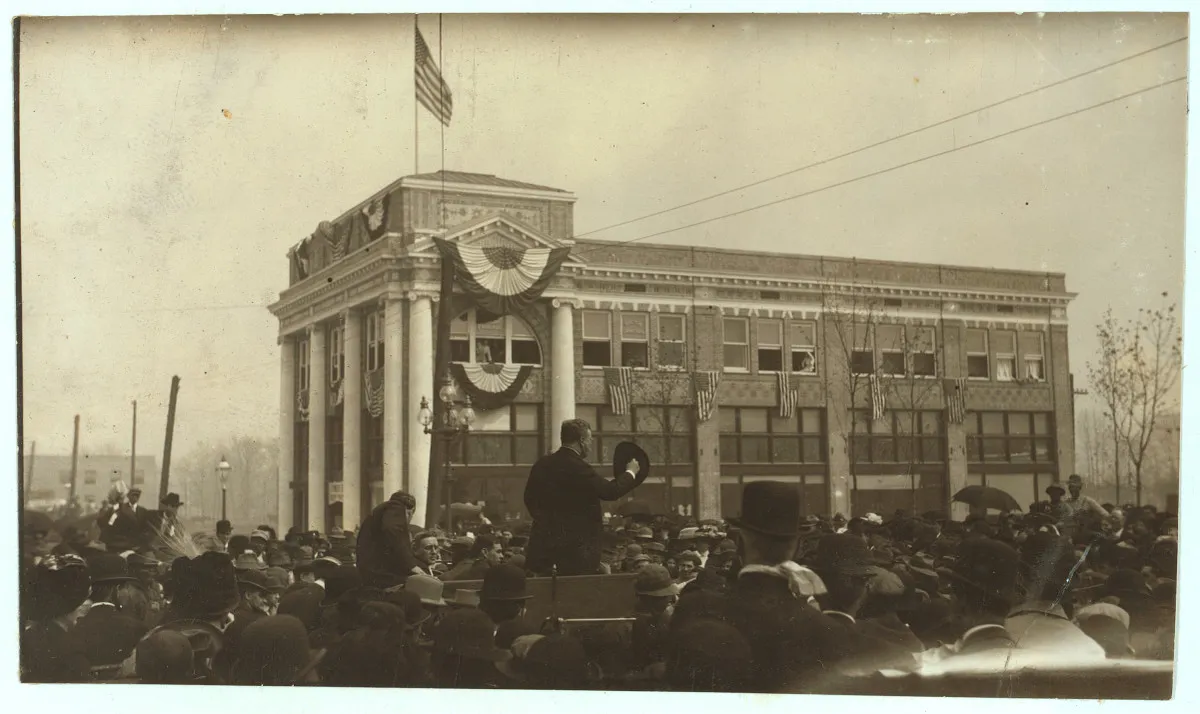 Colonel Theodore Roosevelt speaking from a bunting-draped platform to a large crowd